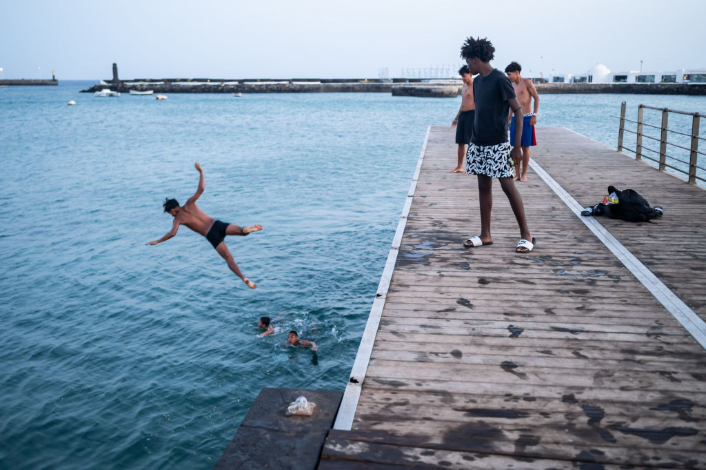 Adolescentes saltando desde un muelle al atardecer en Arrecife, Lanzarote, Islas Canarias.