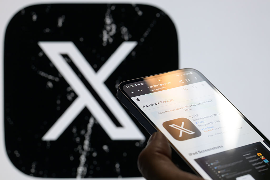 Un móvil inteligente muestra el icono actualizado de la aplicación X en la tienda Apple, con el antiguo icono X visible al fondo.