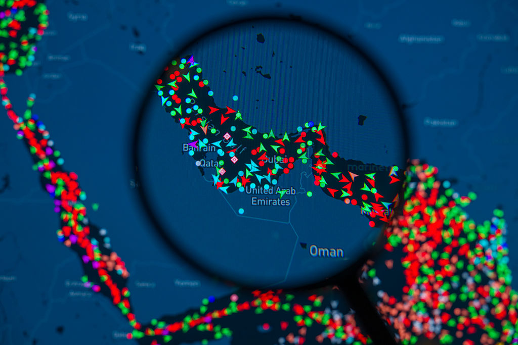 Ilustración fotográfica que muestra un mapa de MarineTraffic con los movimientos de los buques en el estrecho de Ormuz a través de una lupa.