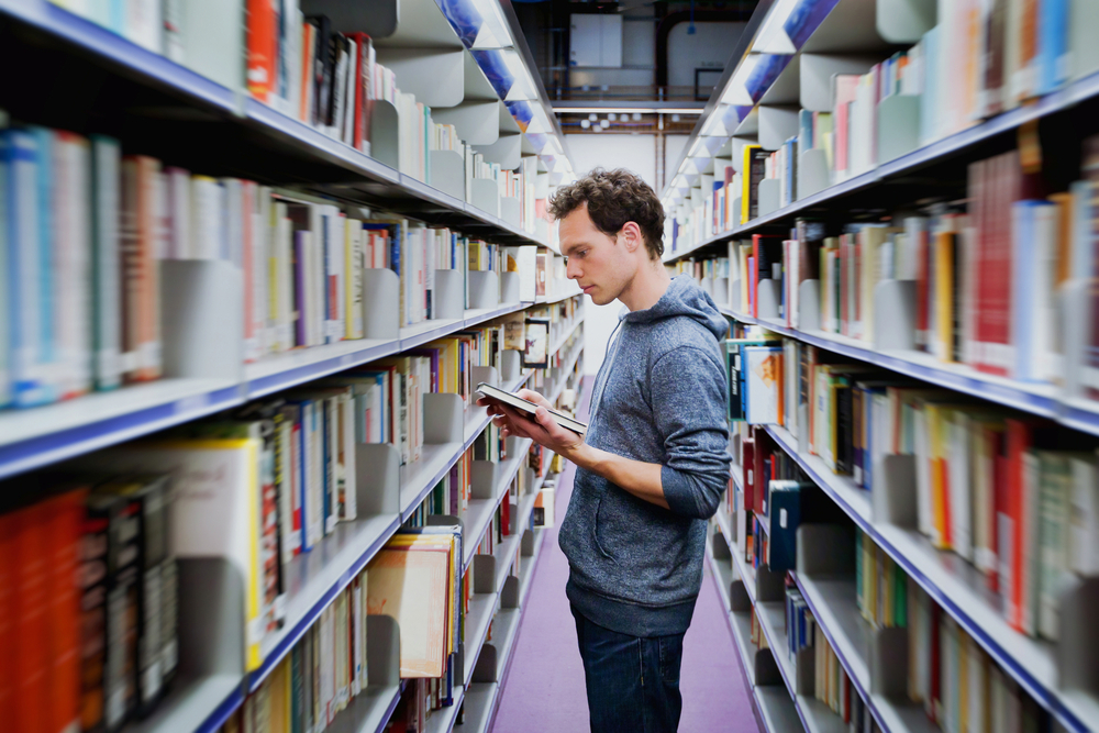 Young,Student,Reading,Book,Between,The,Shelves,In,The,Library