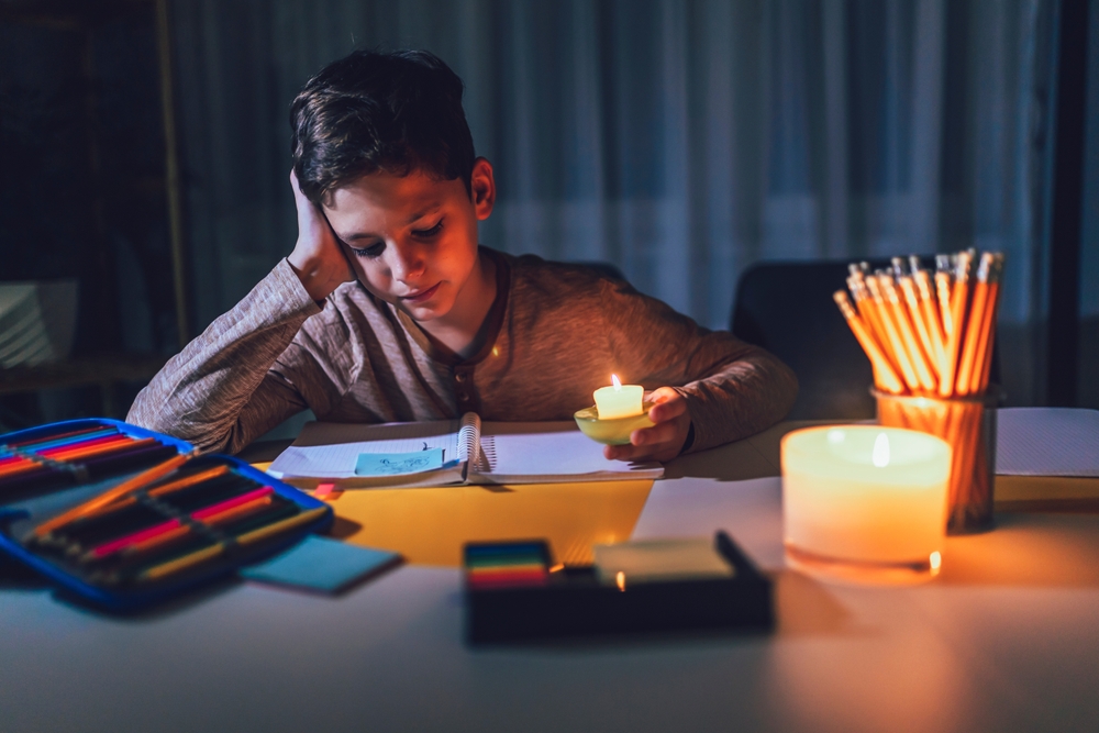 Little,Boy,Studying,In,Low,Light,With,A,Burning,Candle.