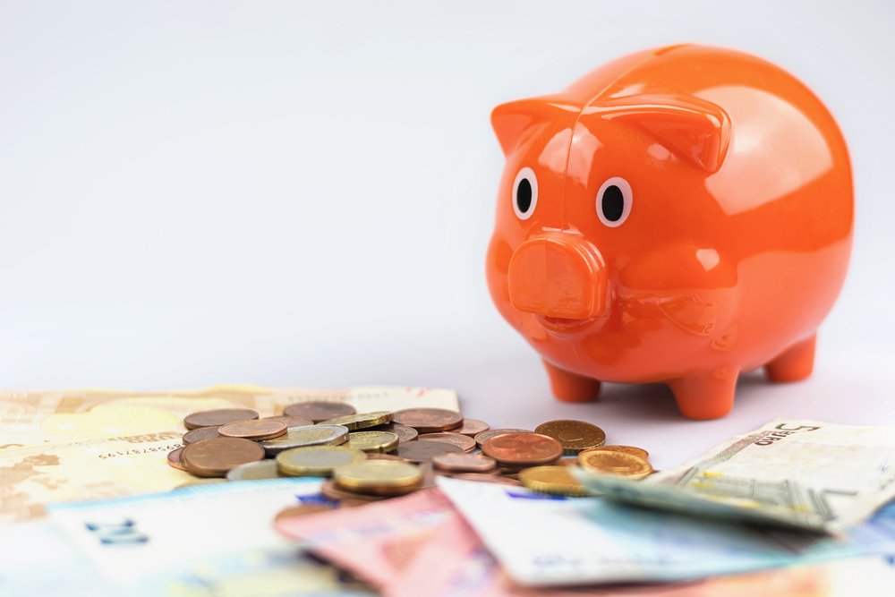 Piggy,Bank,Watching,A,Stack,Of,Euro,Banknotes,And,Coins.