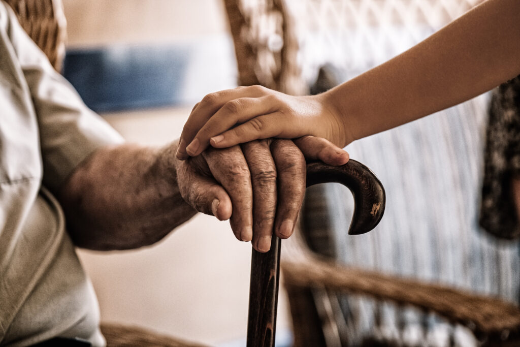 child&rsquo;s hand over old man&rsquo;s hand holding a cane.