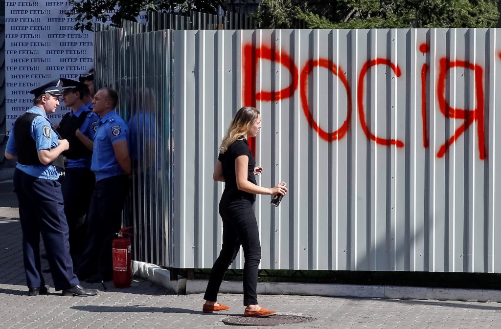 Police stand guard as an activist sprays the word ‚Russia‘ on the barrier around Ukrainian television channel „Inter,“ which protesters say has an anti-Ukrainian stance, in Kiev
