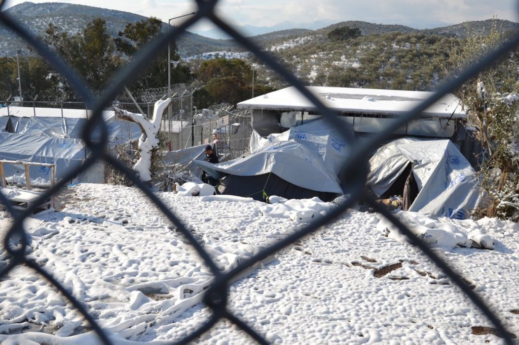 epa05705073 Refugees walk in the snow behind a fence at the Moria refugees camp on Lesvos Island, Greece, 08 January 2017. A cold wave across Greece causing temperatures to drop drastically brought snowfall to many cities.  EPA/STRATIS BALASKAS