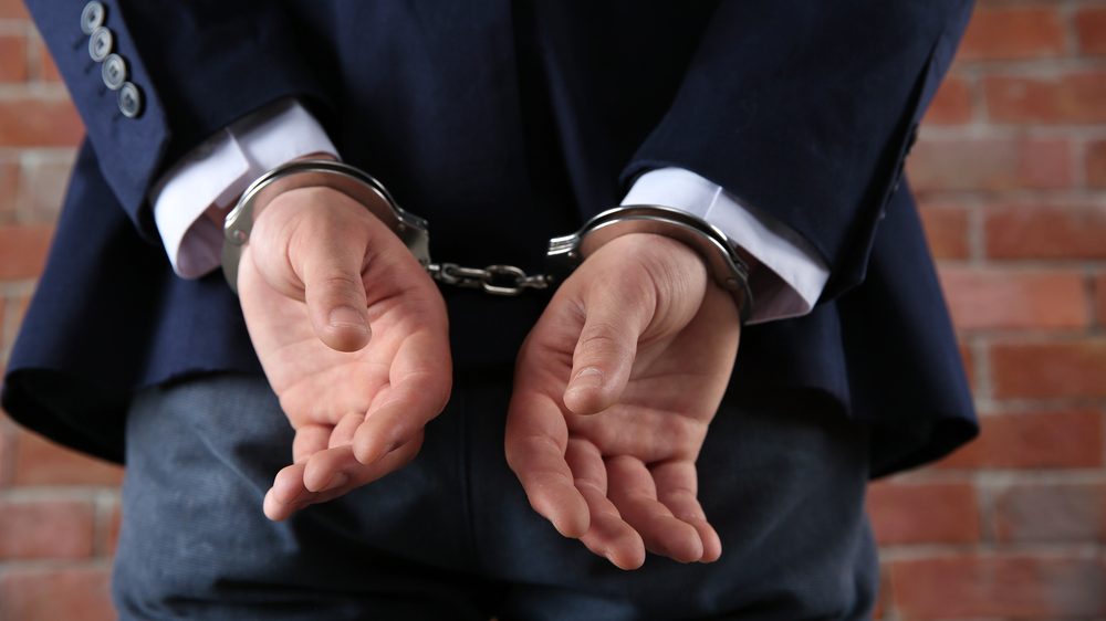 Man,In,Handcuffs,On,Brick,Wall,Background