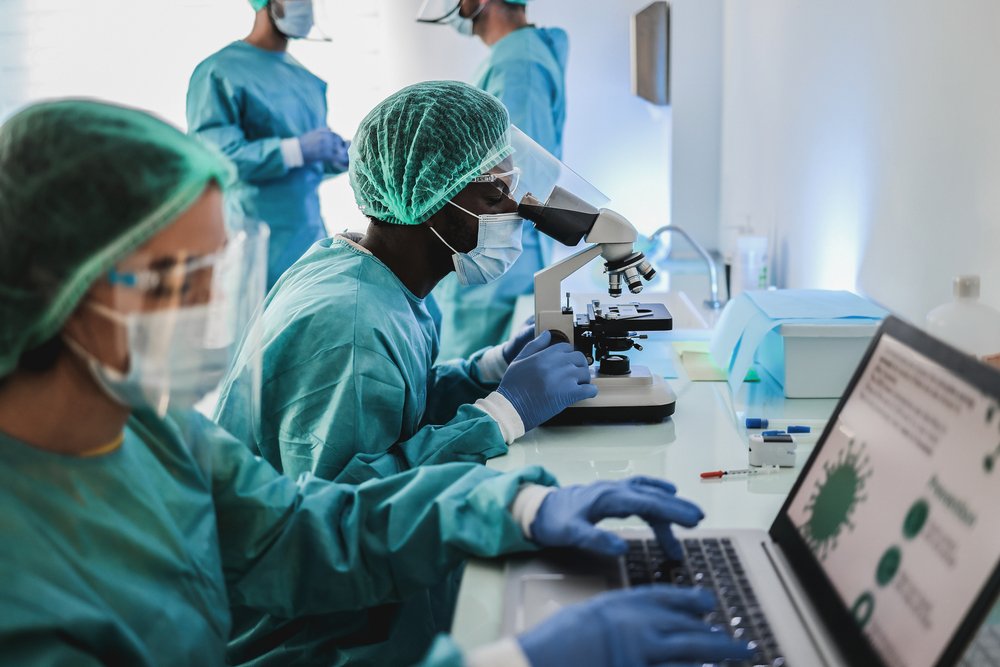 Multiracial,Medical,Scientists,In,Hazmat,Suit,Working,With,Microscope,And