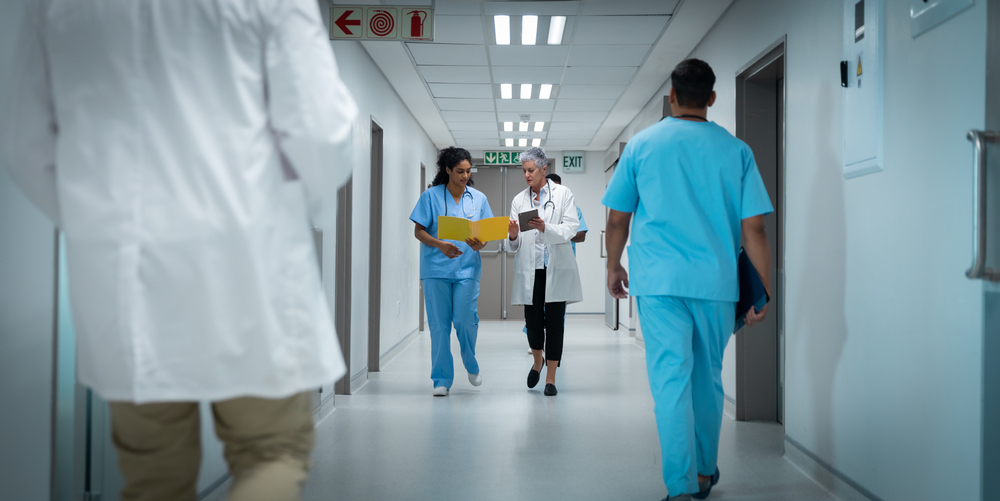 Diverse,Couple,Of,Female,Doctors,Walking,Through,Hospital,Corridor,Discussing.
