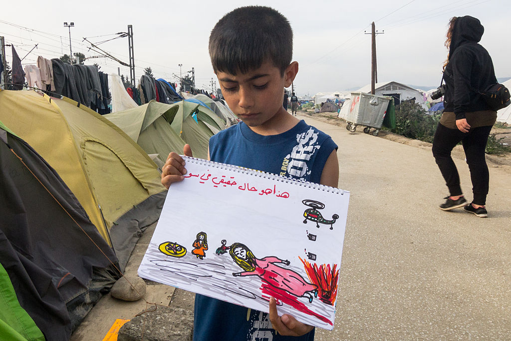 A Syrian boy shows a painting book at the camera, where he